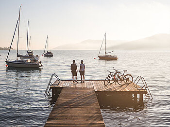 2 Radfahrer auf einem Steg am Attersee, Segelboote in der Abenddämmerung