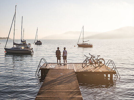 2 Radfahrer auf einem Steg am Attersee, Segelboote in der Abenddämmerung