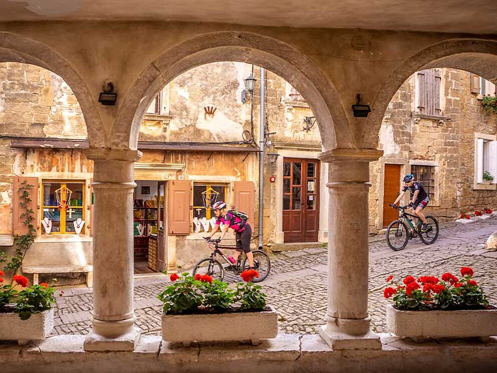 Alte Gewölbe mit Blumenkästen, im Hintergrund Biker in einer schmalen Gasse