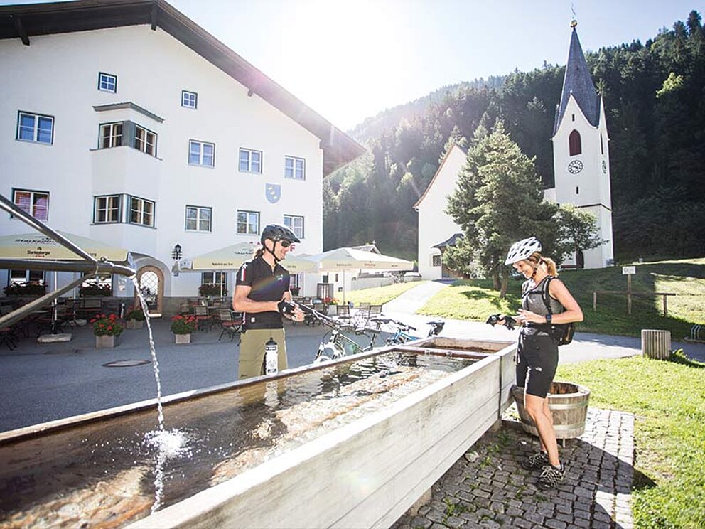 2 Bikerinnen beim Brunnen füllen ihre Wasserflaschen auf