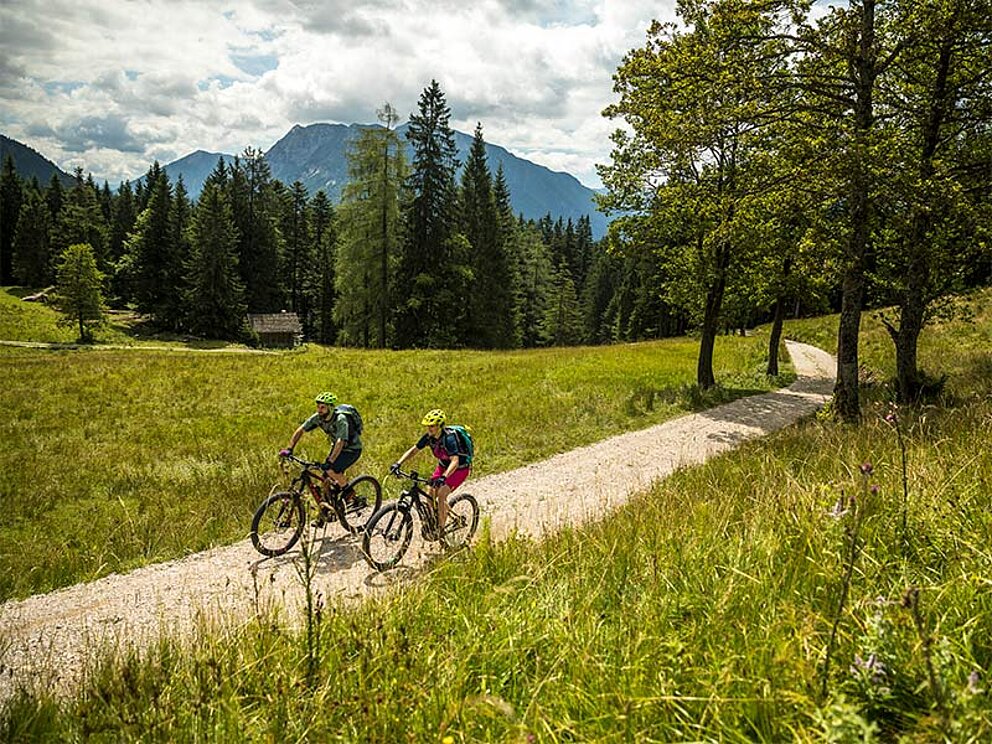 Paar radelt im MTB Urlaub über eine herbstliche Almwiese 