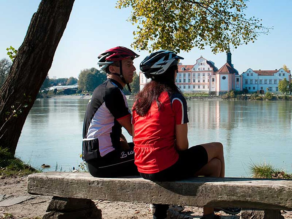 Radfahrerpaar am Inn auf Bank mit Blick auf Schärding