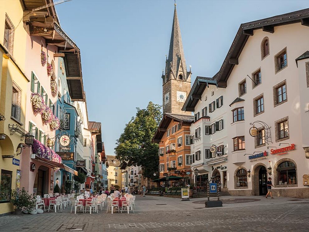 Platz in Kitzbühel mit Kirchen und Geschäften.