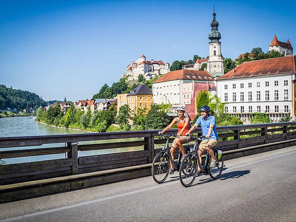 2 Radfahrer auf der Salzach-Brücke, im Hintergrund die Stadt mit Kirchturm