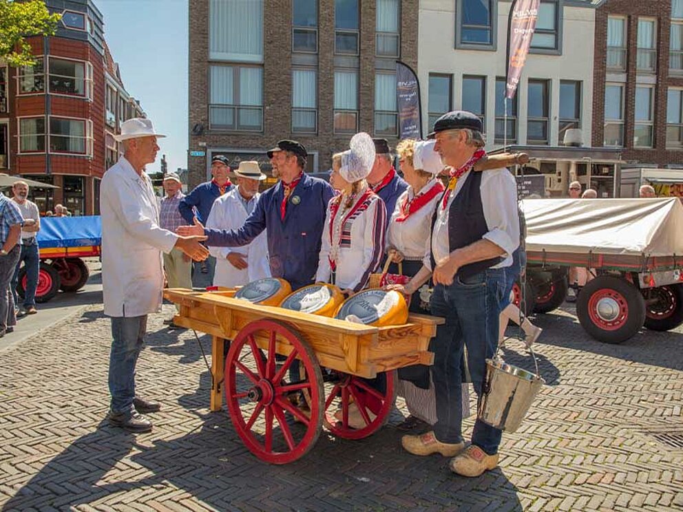 ein Gruppe von Mark-Verkäufern in holländischer Tracht mit einem Verkaufswagen mit Käse