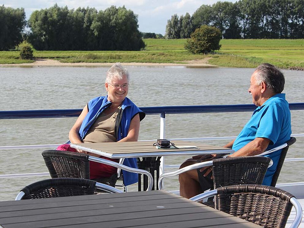 2 Männer sitzen bei Tisch am Oberdeck