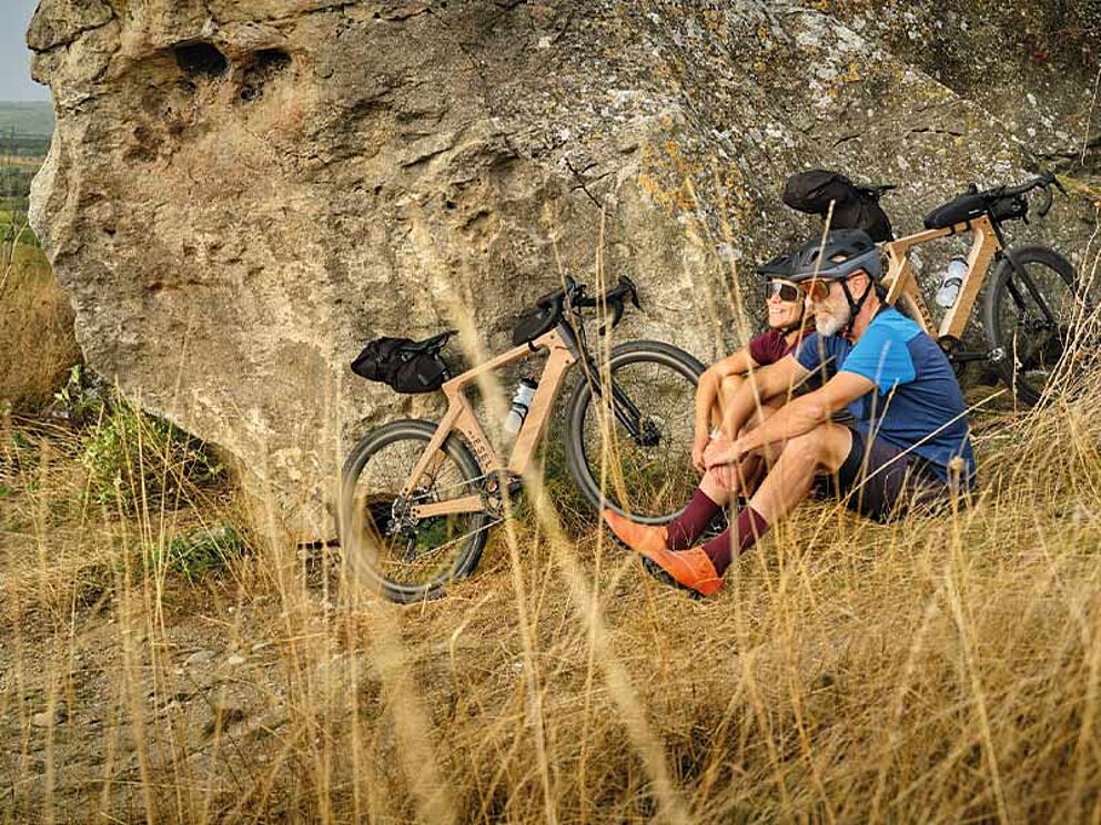 2 Biker sitzen in der Wiese, ihre Gravelbikes an einen Felsen gelehnt.