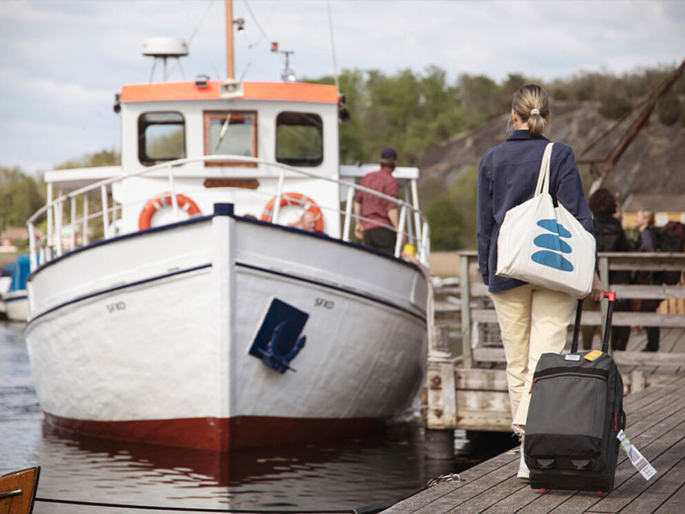 Eine Dame geht mit Ihrem Koffer richtung Schiff im Hafen