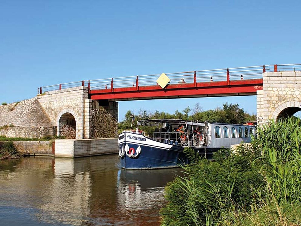 Schiffsansicht L'Estello von vorne in Fahrt auf einem Fluss in Frankreich, unter einer Brücke durch