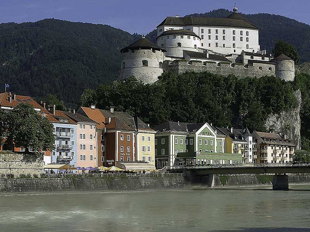 Die Festung Kufstein thront hoch über dem Inn. Am Flussufer reihen sich bunte Häuser aneinander.