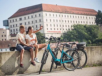 Zwei E- Biker machen Pause am Donauradweg - im Hintergrund das Schloss Linz