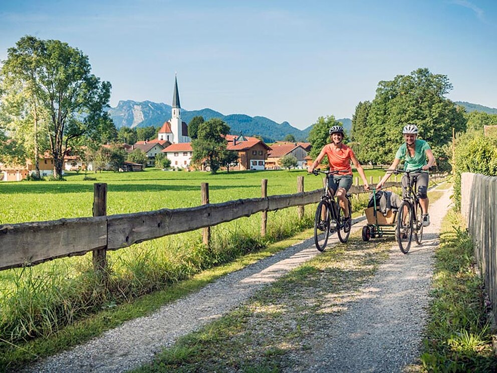 Eltern und Kleinkind auf Fahrrädern unterwegs auf einem Güterweg im Grünen.