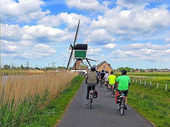 Radfahrer am asphaltierten Radweg auf eine Windmühle zufahrend