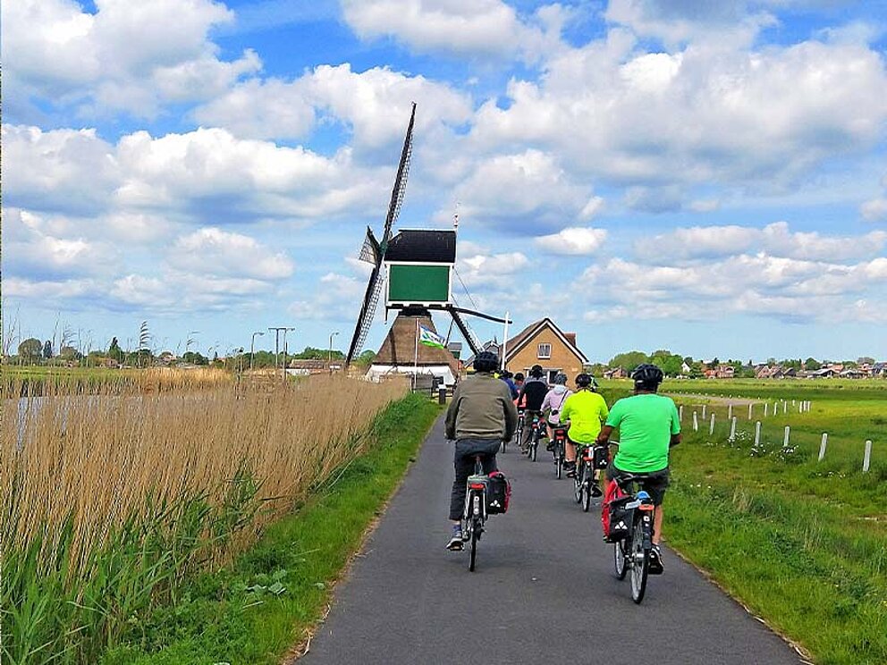 Radfahrer am asphaltierten Radweg auf eine Windmühle zufahrend