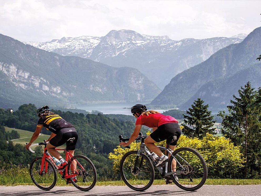 2 Gravelbiker rollen talwärts vom Predigtstuhl, im Hintergrund der Hallstätter See und Berge