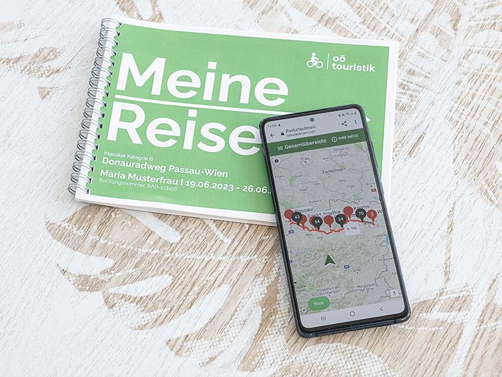 ein Smartphone mit der Navi-Anwendung und das Routenbuch auf einem Tisch liegend