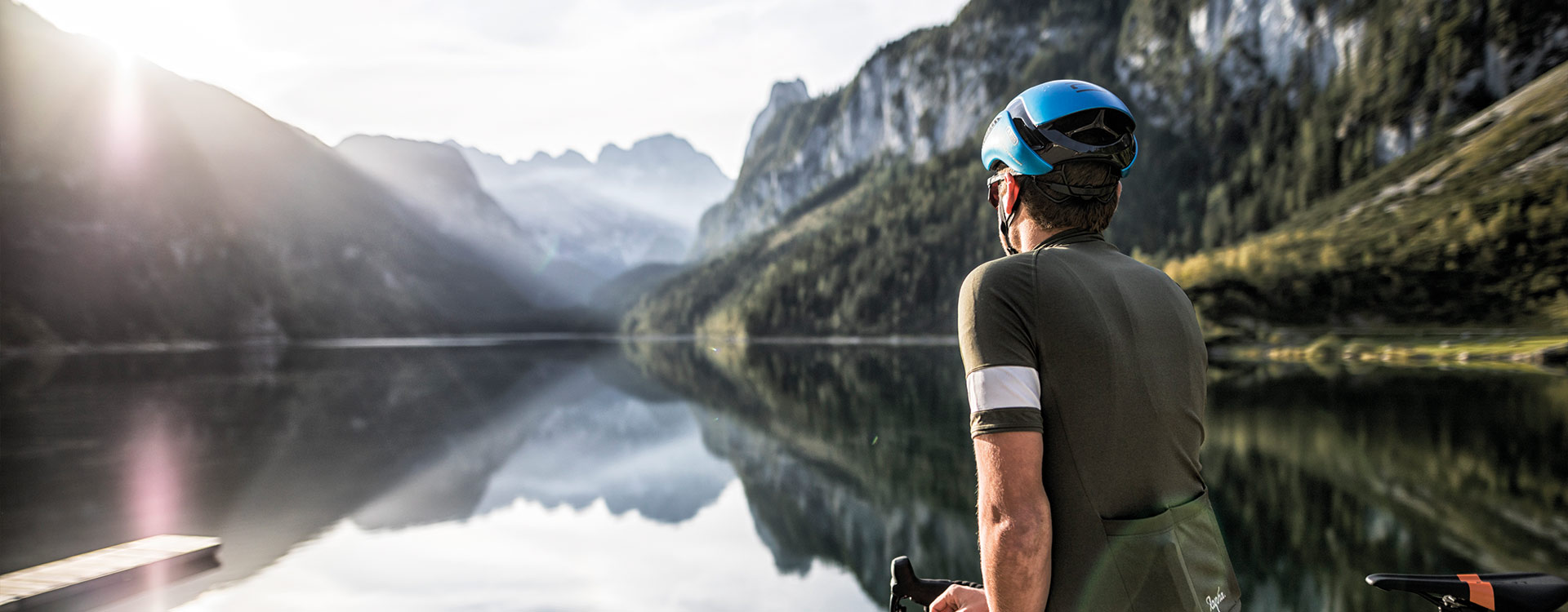 Ein Gravelbiker steht am Ufer des Gosausees und blickt in Richtung des Dachsteins