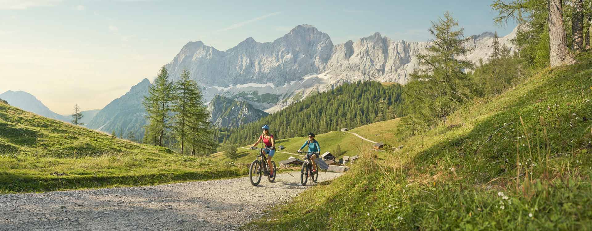 2 Biker auf einem Schotterweg, im Hintergrund der Dachstein