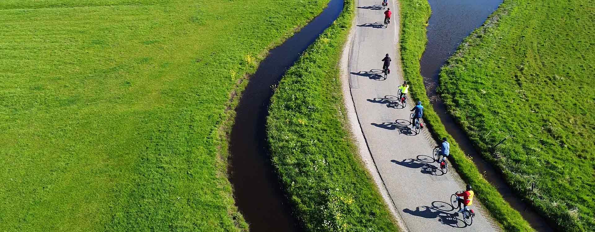 eine Gruppe Radfahrer am Flachen Radweg entlang eines Baches.