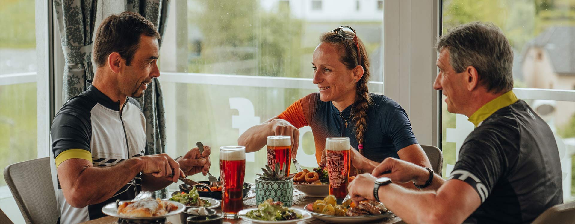 3 Personen am Tisch mit Bier und kulinarischen Köstlichkeiten.