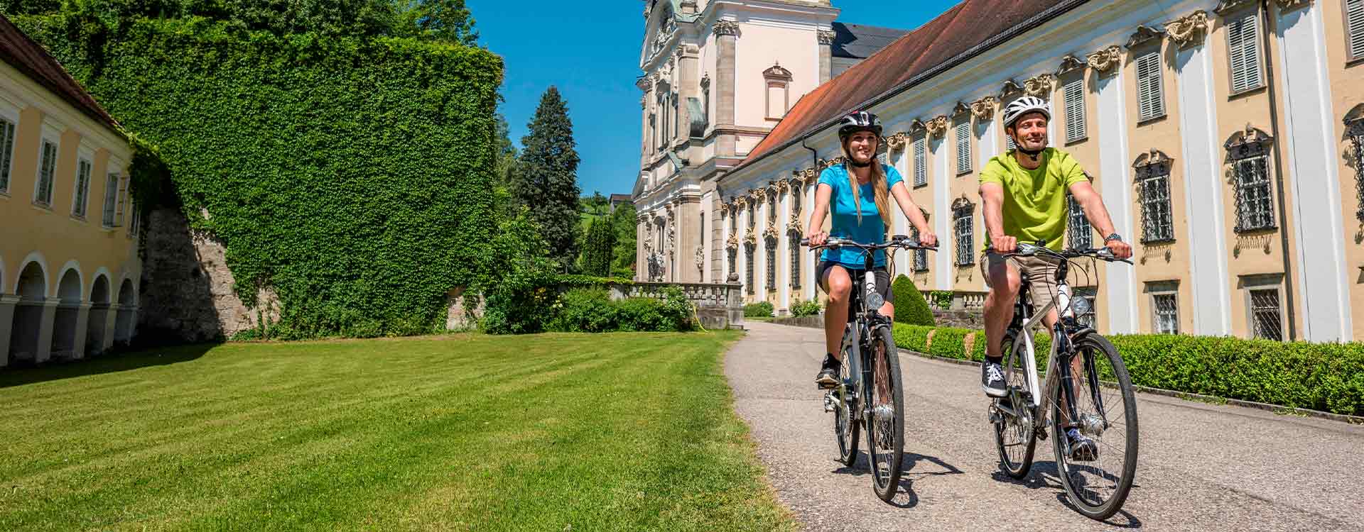 1 Paar radelt durch den Stiftsgarten, im Hintergrund das Stift St. Florian