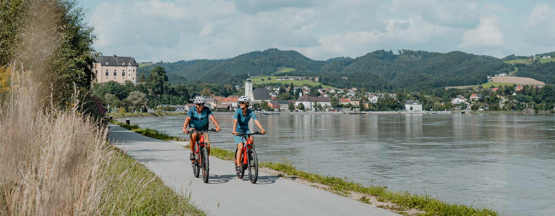 2 Radfahrer am Donauradweg direkt am Donauufer, im Hintergrund die Greinburg