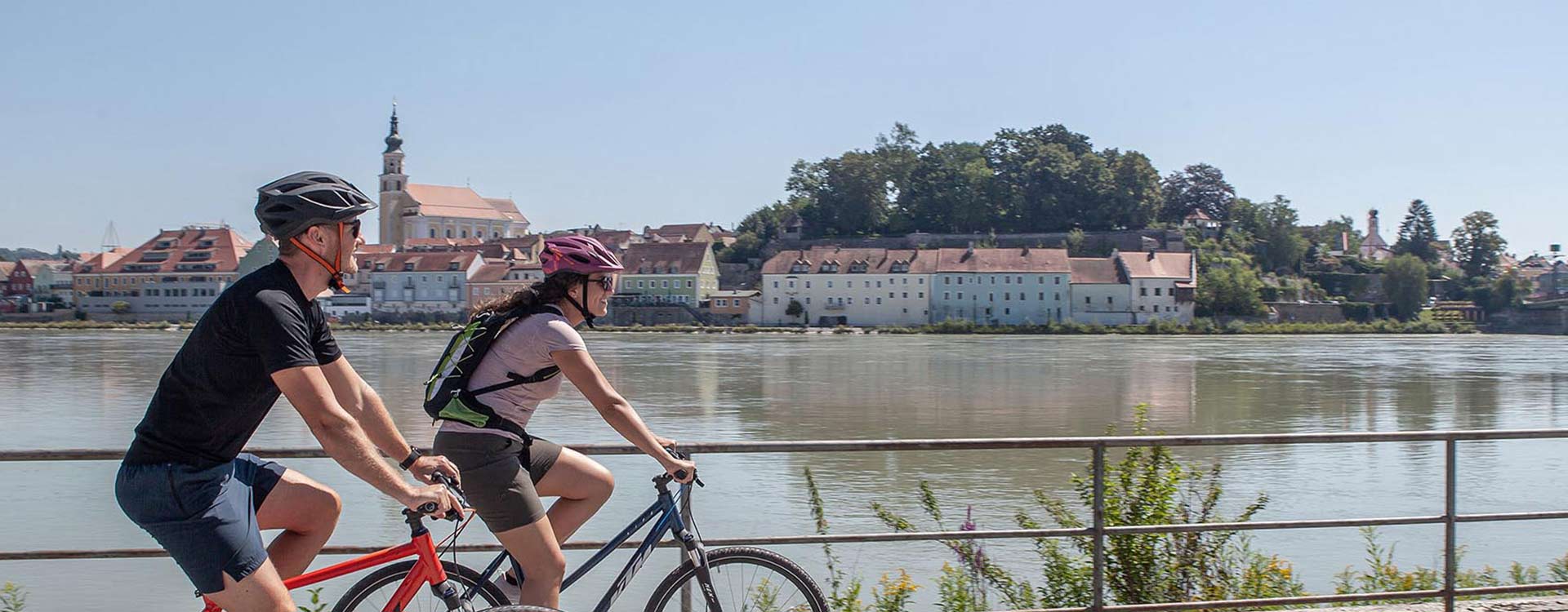 2 Radfahrer am Ufer des Inn, im Hintergrund die Stadt Schärding