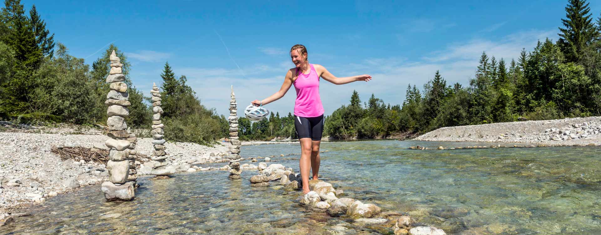 Eine Dame balanciert barfuß auf Steinen am Isar-Ufer