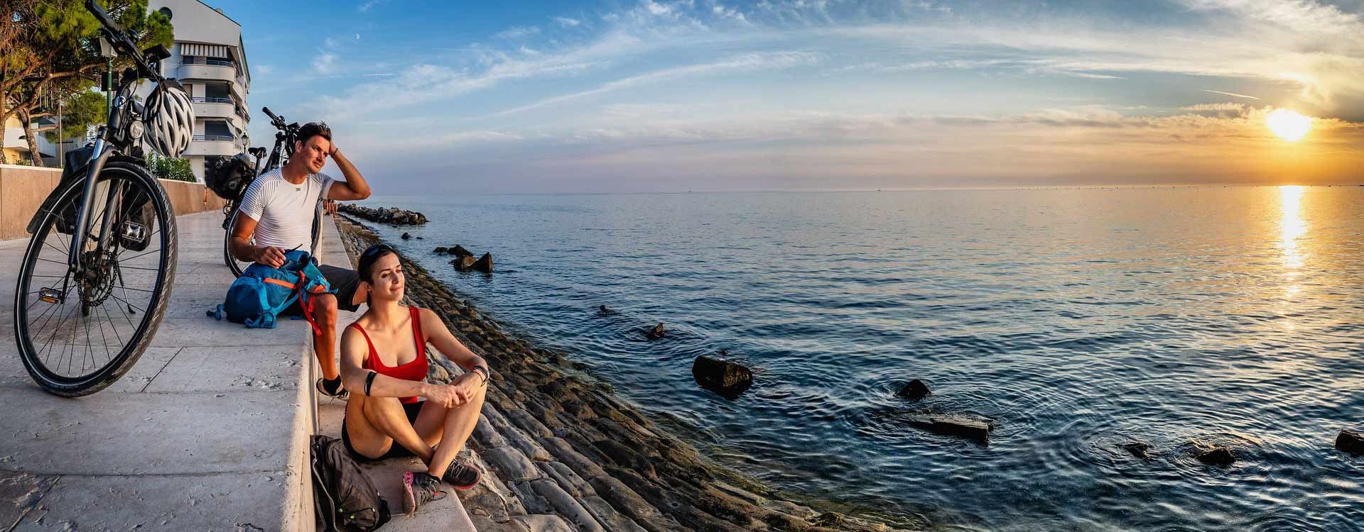 2 Personen sitzen am Meeresufer im Sonnenuntergang