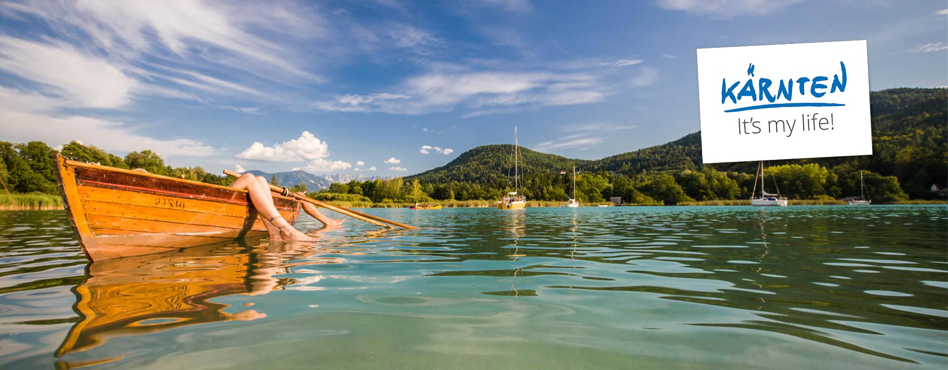 Ein Ruderboot am Wörthersee, 2 Beinpaare hängen vom Boot aus ins Wasser.