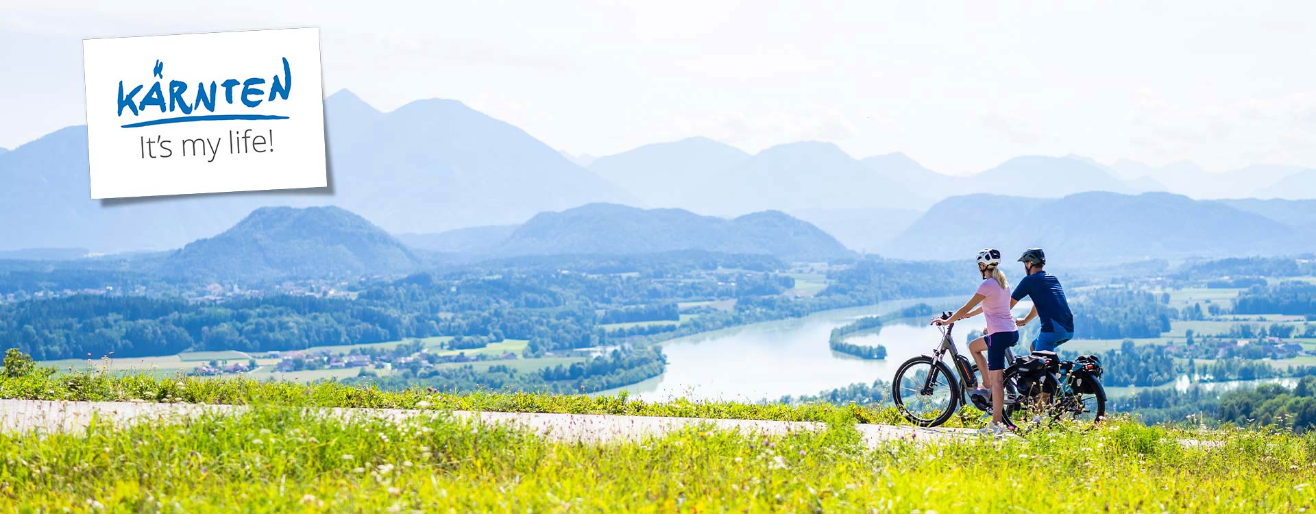2 Radfahrer vor einer Kulisse aus Berg- und Seepanorama