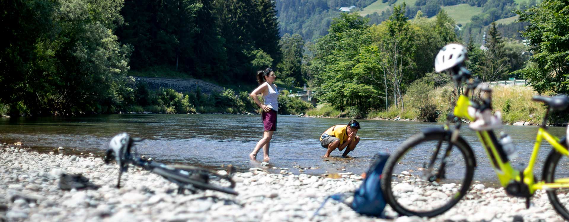 2 Radfahrer kühlen sich am Murufer ab, die Räder stehen im Vordergrund im Flussbett
