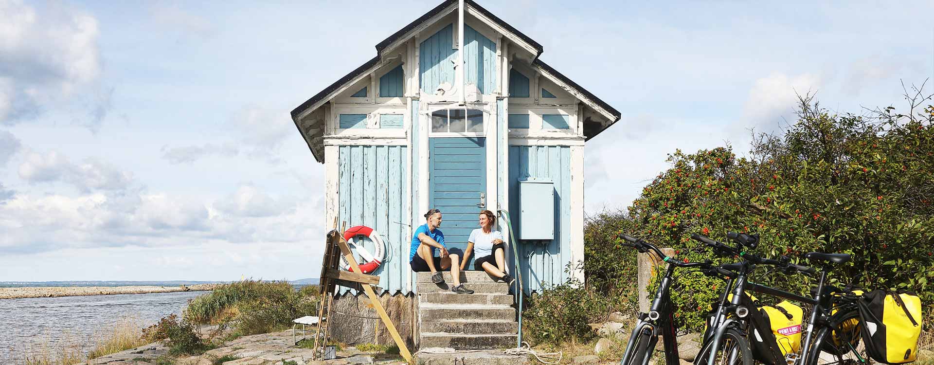 2 Personen sitzen auf der Treppe zu einem kleinen Strandhäuschen 