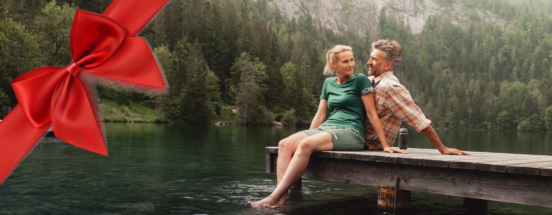 ein Paar sitzt auf einem Steg und lässt die Beine ins Wasser baumeln.